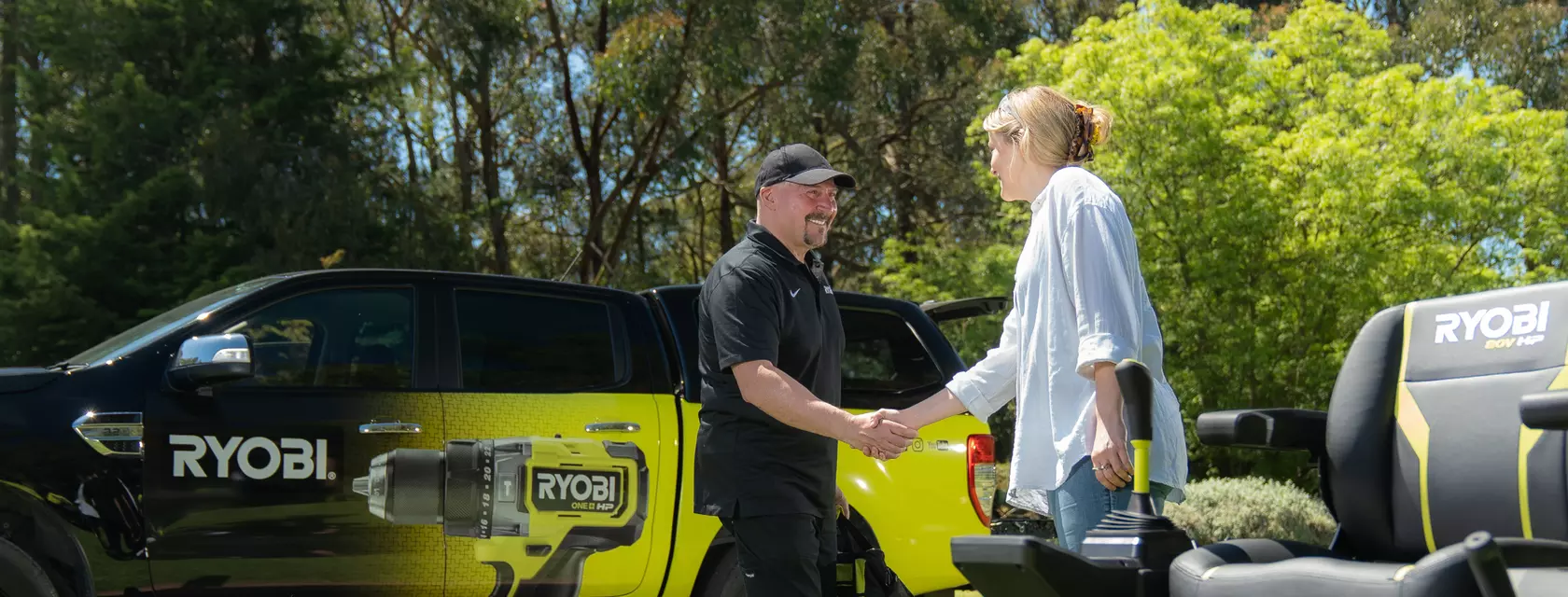 Man shaking hands with woman in front of RYOBI ute and ride on mower